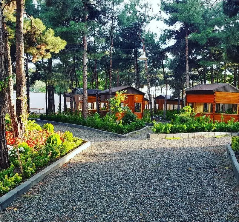 باغ رستوران بهشت پنهان، فضایی دلنشین با کلبه‌های چوبی دنج میان درختان بلند و مسیرهای سنگی زیبا، مناسب برای تجربه غذایی خاطره‌انگیز.