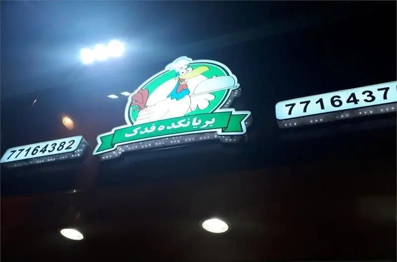 تابلوی روشن فست فود فدک با لوگوی سرآشپز مرغی، نام «بریان کده فدک» و شماره تماس‌های 77164382 و 7716437 برای سفارش.