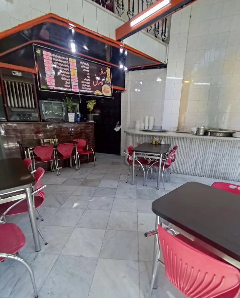 نمای داخلی از طباخی کاشانی، یک رستوران سنتی با دکوراسیون ساده و میز و صندلی‌های قرمز برای سرو کله‌پاچه و دیگر غذاهای ایرانی.