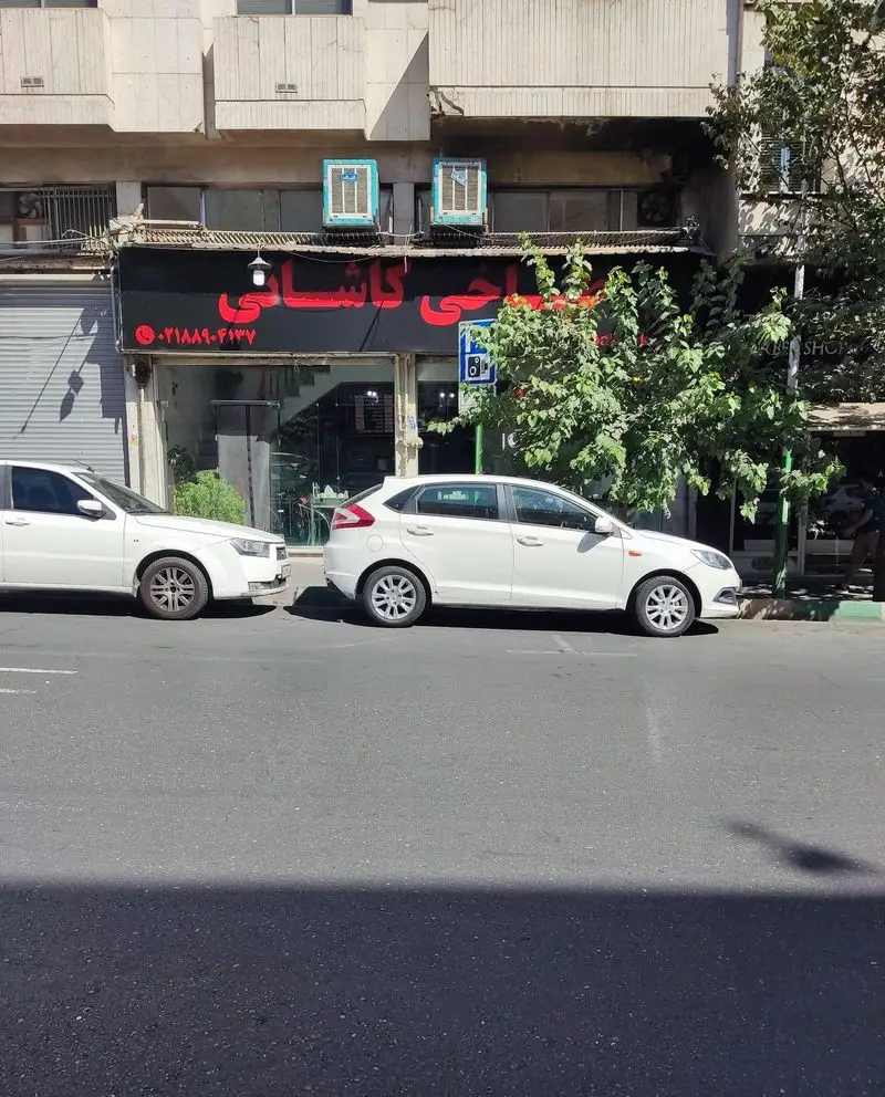 نمای بیرونی طباخی کاشانی، شامل سردر با نام تجاری و شماره تلفن ۰۲۱۸۸۸۰۴۱۳۷ در خیابان، با دو خودروی سفید پارک شده