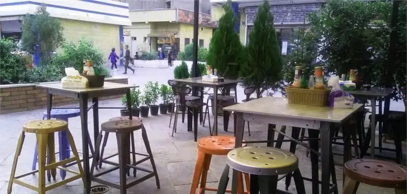 محیط بیرونی دنج و مدرن پیتزایی پادلا با میزهای بلند و صندلی‌های استیل متنوع، ایده‌آل برای لذت بردن از پیتزا و لحظات خوب.