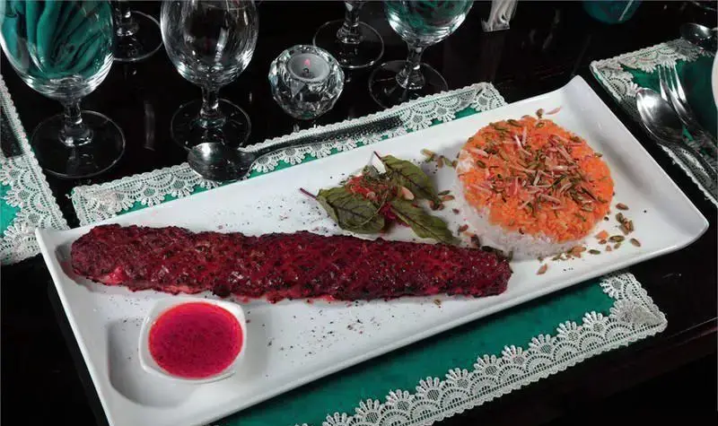 غذای اصیل مراکشی و الجزایری شامل کباب قرمز و برنج زعفرانی با مغزها، چیده شده بر میزی زیبا در محیط دلنشین رستوران مراکش الجزایر برای شامی فراموش‌نشدنی.