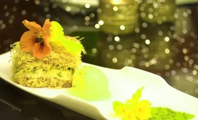 دسر سنتی کادایف مراکشی-الجزایری با بستنی سبز و تزئینات گل، روی بشقاب سفید در فضای دلنشین رستوران ما. طعمی خاص و لذیذ.