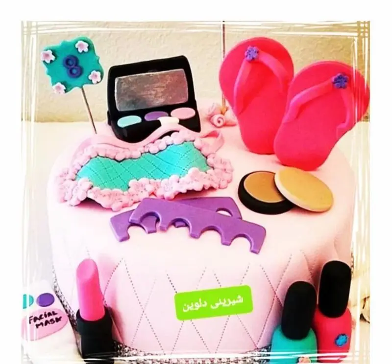 کیک تولد فوندانت زنانه شیرینی دلوین با دکور لوازم آرایش و فشن شامل رژلب، لاک ناخن، بیکینی و صندل‌های صورتی.