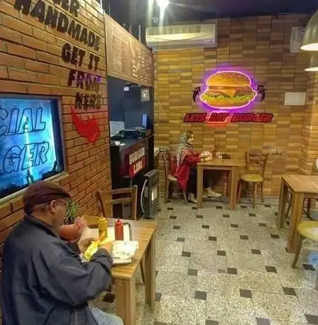 فضای داخلی دنج فست فود برگر لاین با دکوراسیون آجری، تابلوی نئونی برگر، و مشتریانی که از همبرگرهای دست‌ساز لذت می‌برند.