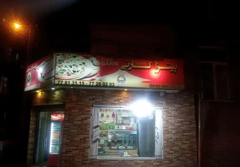 نمای شبانه پیتزا گارنی، کسب و کار فست فود با تابلوی روشن نمایش دهنده پیتزا و شماره تلفن‌های تماس برای سفارش.