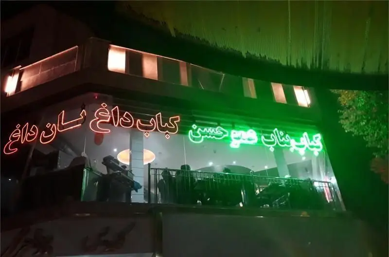 کبابی کباب عموحسن در شب با تابلوی نئون کباب داغ و نان داغ، نمای بیرونی یک رستوران سنتی ایرانی با نورپردازی جذاب.