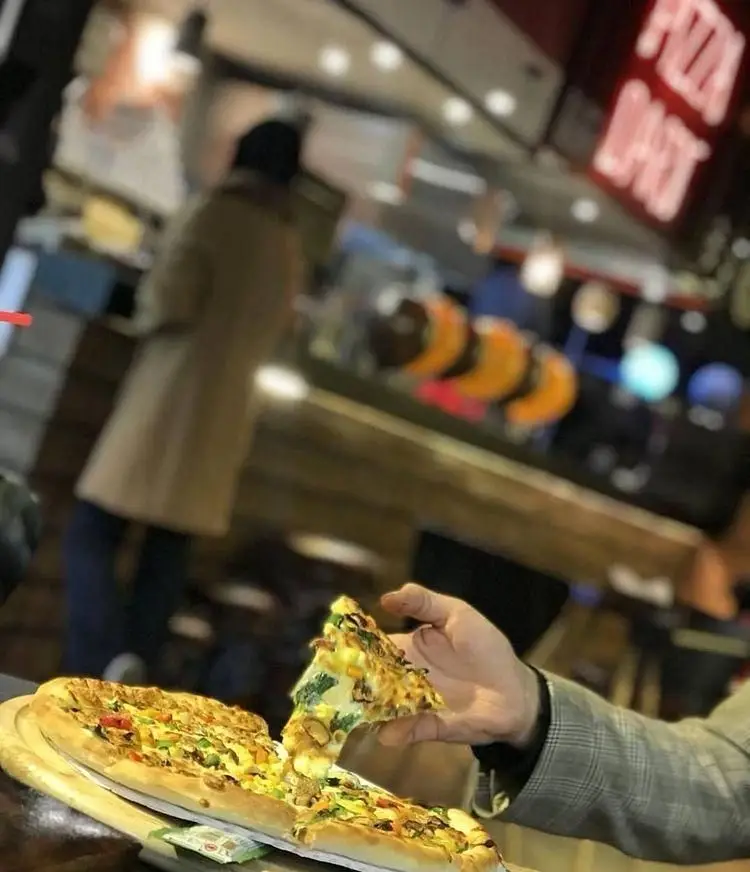 پیتزای جذاب و پر سبزیجات فست فود پیتزا دارت در دستان مشتری، نشان‌دهنده تجربه غذایی لذت‌بخش در محیطی دلپذیر.