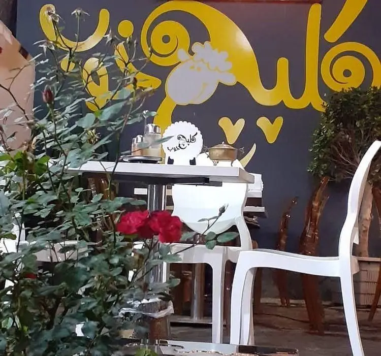 فضای داخلی زیبا و آرامشبخش طباخی کلپچ خوب، با طراحی منحصربهفرد، دیوارنگاره خلاقانه، میز و صندلیهای مدرن و گلدانهای گل رز قرمز.