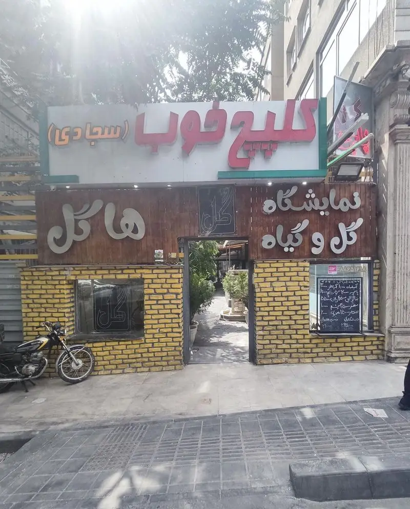 طباخی کلپچ خوب (سجادی) با نمای آجری، تابلوی قرمز و ورودی گل و گیاه، مکانی دلپذیر برای سرو کلهپاچه در تهران.