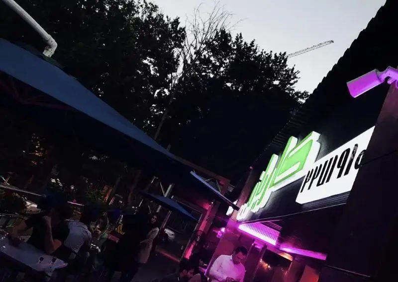 نمای شب از فضای باز و زیبای رستوران فرنگی کاریان با تابلو روشن، مشتریان در حال لذت بردن از غذا و چترهای بزرگ آبی.