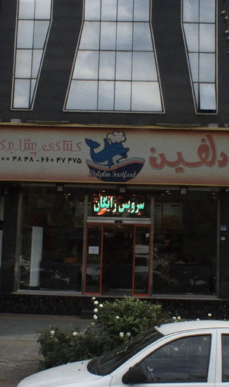 نمای خارجی فست فود پیتزا دلفین: تابلوی رستوران با لوگوی دلفین سرآشپز، ارائه انواع پیتزا، کنتاکی، برگر و سرویس رایگان.