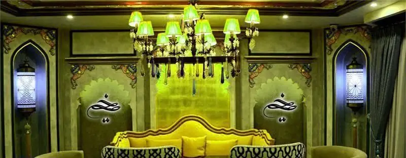 نمایی از دکوراسیون داخلی رستوران عربی خیمه با مبلمان زرد، لوسترهای پرنور، فانوس‌های سنتی در طاقچه‌های قوسی و دیوارنگاره‌های شرقی.