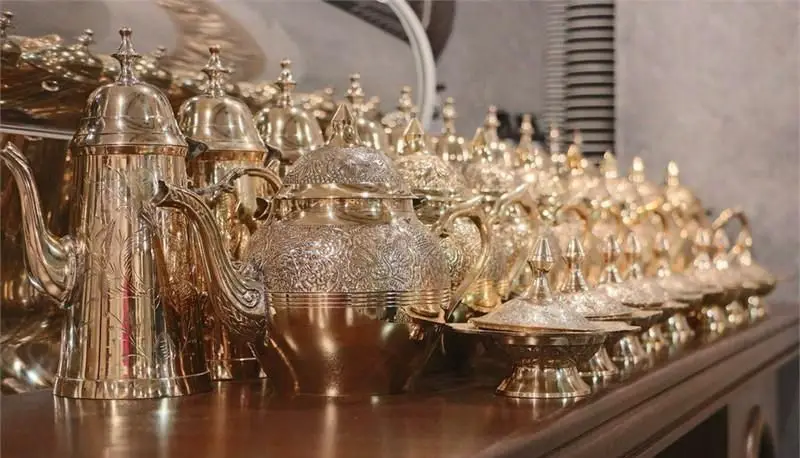 قوری‌ها، قهوه‌جوش‌ها و ظروف دردار برنجی و طلایی رنگ با نقوش زیبا در چیدمان سنتی، مناسب برای پذیرایی در رستوران عربی خیمه.