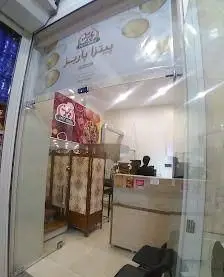 تصویر کامل از نمای بیرونی و ورودی شیشه‌ای فست فود پیتزا پاریز. دکوراسیون داخلی ساده با کانتر سفارش و محیط انتظار مشتریان.