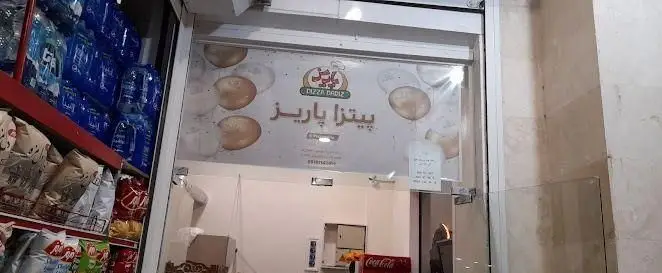 ورودی جذاب فست فود پیتزا پاریز، نمایانگر تابلو و لوگوی برند، به همراه قفسه‌های پر از نوشیدنی و تنقلات آماده فروش.