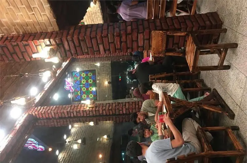 تصویری از داخل کبابی جگرسرای دولت: مشتریان در حال صرف غذا، میز و صندلی‌های چوبی، دیوارهای آجری و پنجره شیشه‌ای رنگی با نورپردازی گرم شب.