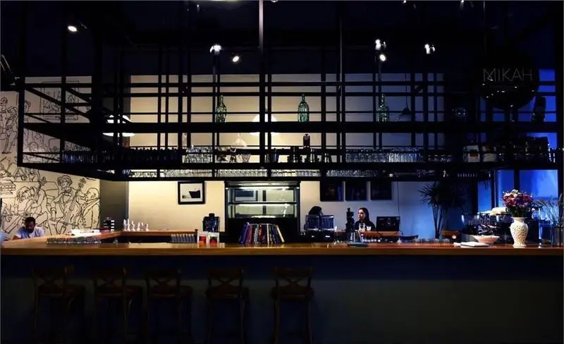 فضای داخلی کافه شبانه روزی اروما با دکوراسیون مدرن، میز بار چوبی، صندلی‌های بلند، قفسه فلزی و نقاشی دیواری هنری موسیقی‌دانان.