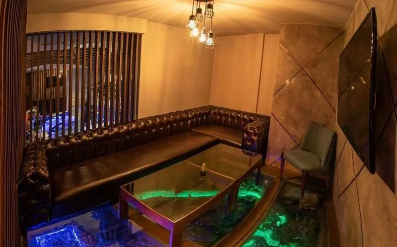 فضای داخلی دنج و لوکس کافه شبانه روزی اروما، شامل مبلمان چرم ال، میز شیشه ای مدرن، نورپردازی خاص کف آبی و سبز و دکوراسیون شیک.