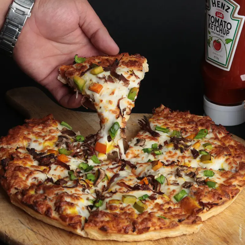 برش پیتزا داغ و خوشمزه نایت مز (شبانه روزی) با پنیر کشدار، قارچ، فلفل دلمه‌ای و کچاپ در کنار آن.