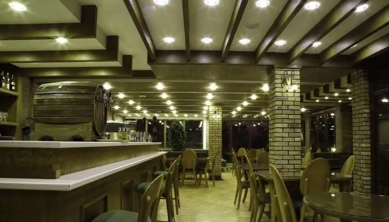 دکوراسیون داخلی رستوران پریماورا: بار چوبی با بشکه بزرگ، ستون‌های آجری، سقف با نورپردازی گرم و میز و صندلی‌های چوبی.