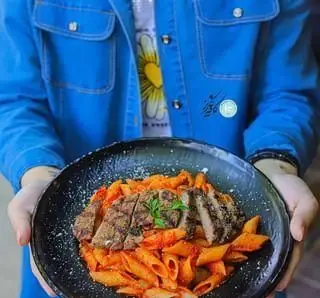 تصویری از سرو پاستا پنه با سس قرمز و برش‌های گوشت گریل شده در کافه رستوران باغ کاریز. یک غذای لذیذ از منوی متنوع.