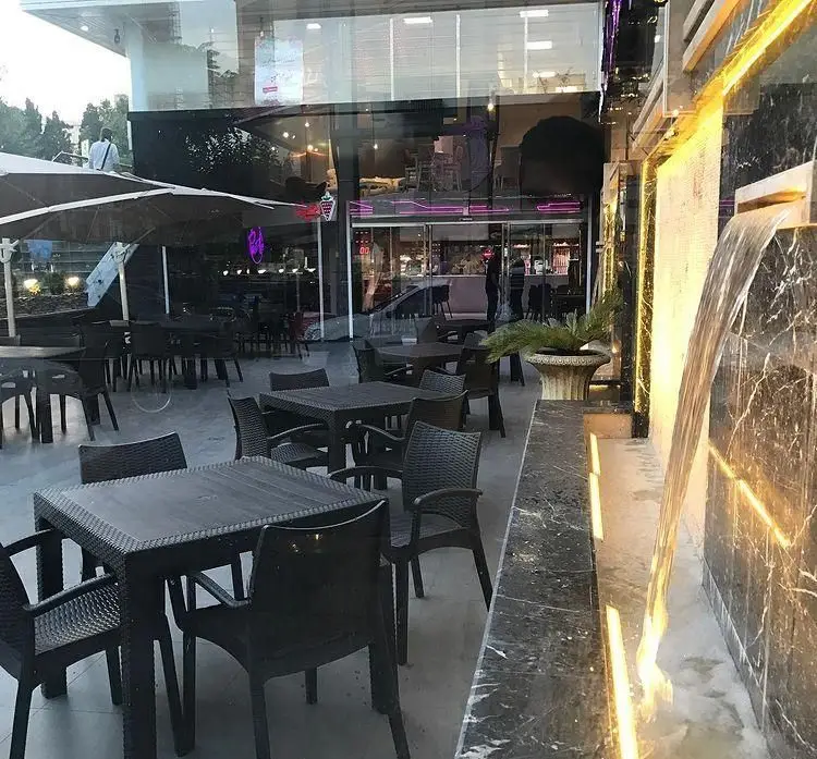 محیط بیرونی و دلباز رستوران پر پل سوخاری، مجهز به میز و صندلی‌های راحت و آبنمای مدرن با نورپردازی گرم.