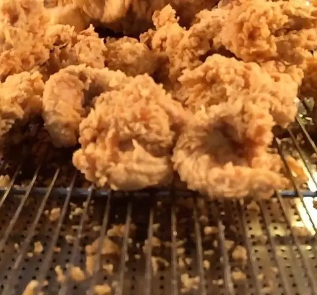 تصویری نزدیک از تکه‌های مرغ سوخاری طلایی و ترد پر پل سوخاری روی توری خنک کننده. لذت طعم واقعی سوخاری با کیفیت بالا.