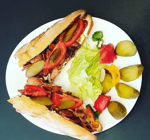 ساندویچ مرغ سوخاری پر پل با قارچ، گوجه و خیارشور در کنار سالاد و ترشی، انتخابی عالی از غذای آماده و خوشمزه.