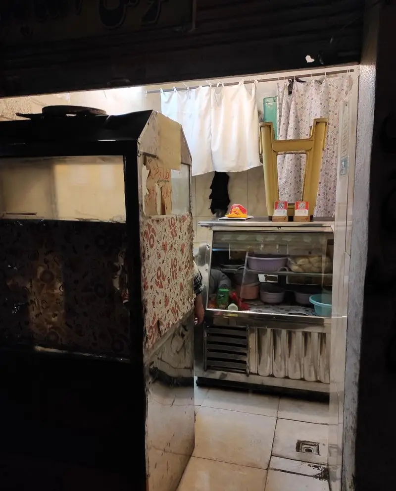 تصویری از ورودی فلافل ابو خلاص کربلایی، شامل پیشخوان سرو غذا، یخچال ویترینی با فلافل و مواد اولیه تازه، فضایی ساده و محلی برای مشتریان.