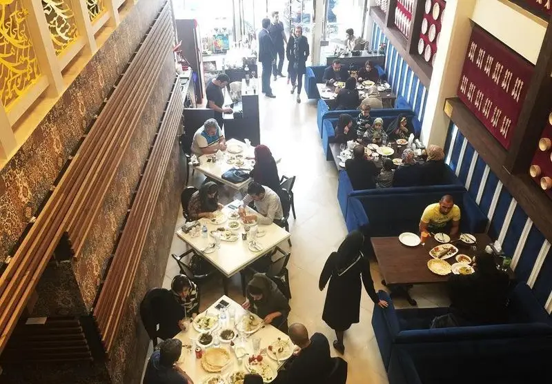 رستوران ماهی سفید با فضایی دلنشین و مشتریان شاد در حال صرف غذا. دکوراسیون داخلی با میزهای چوبی و غرفه‌های آبی رنگ جذاب.