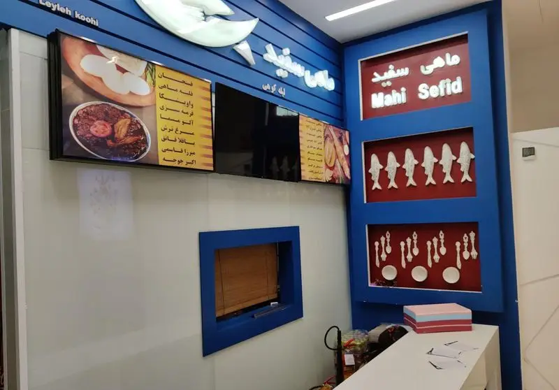 فضای داخلی رستوران ماهی سفید، با تابلوهای منوی غذاهای محلی گیلانی و دکوراسیون آبی و سفید زیبا برای جذب مشتری.