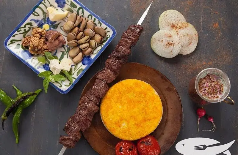 یک میز شام کامل ایرانی: کباب با برنج زعفرانی، ته دیگ، گوجه، پیاز و مخلفات تازه مانند باقالی، گردو و پنیر در رستوران ماهی سفید.
