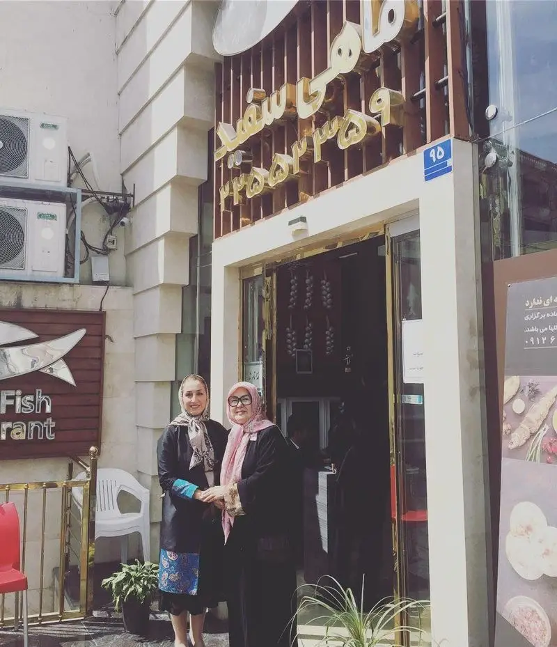 نمای ورودی رستوران ماهی سفید در تهران با تابلوی نام، آدرس (پلاک 95) و شماره تلفن 23552235، و دو خانم در حال ورود. بهترین رستوران غذاهای دریایی.