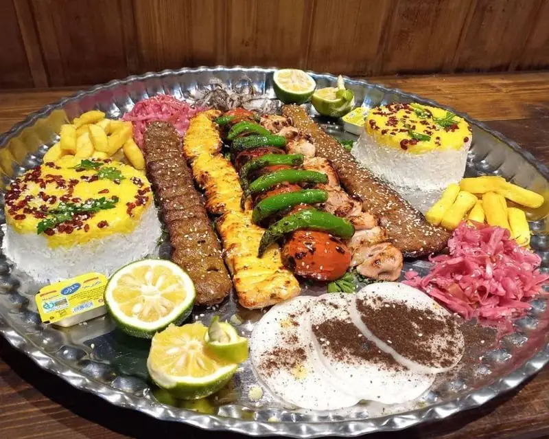 سینی غذای سنتی شامل کباب کوبیده و جوجه، پلو زعفرانی، سیب زمینی و مخلفات در سفره خانه و کافه روستای دیلمان.