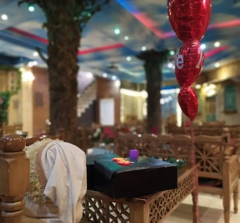 فضای داخلی سفره خانه و کافه روستای دیلمان با دکوراسیون سنتی و خاص، سقف آبی، درختان داخلی و بادکنک‌های قرمز، محیطی دلنشین و رمانتیک.