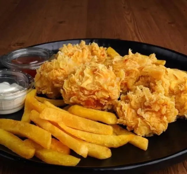 یک بشقاب مشکی شامل مرغ سوخاری ترد و سیب زمینی سرخ کرده طلایی تله پیتزا همراه با سس‌های مخصوص، آماده برای سفارش غذای خوشمزه.