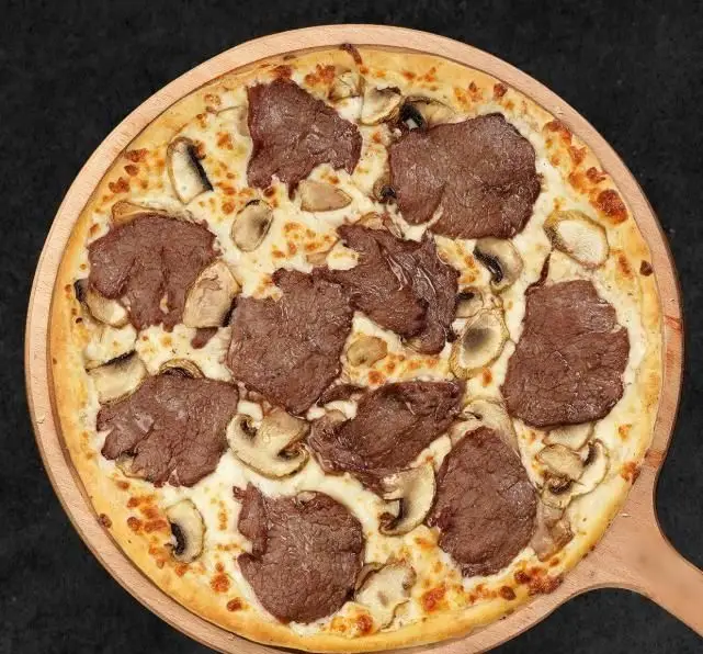 پیتزا گوشت و قارچ تله پیتزا، یک غذای فست فود لذیذ با خمیر پیتزای ترد، سس سفید، تکه‌های گوشت برشته و قارچ تازه روی تخته چوبی.