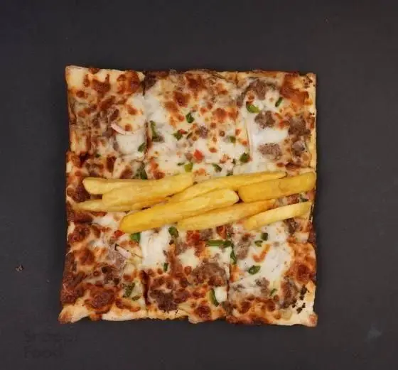 پیتزا گوشت و پنیر تله پیتزا با سیب زمینی سرخ کرده روی آن، یک غذای خوشمزه و پرطرفدار فست فود با برش مربع.