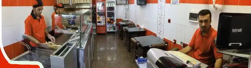 تصویری پانوراما از پیتزا ونیز، نمایشگر آشپزخانه پرکار و کارکنان مجرب در حال تهیه پیتزاهای لذیذ و ساندویچ‌های تازه در محیطی دلنشین و تمیز.