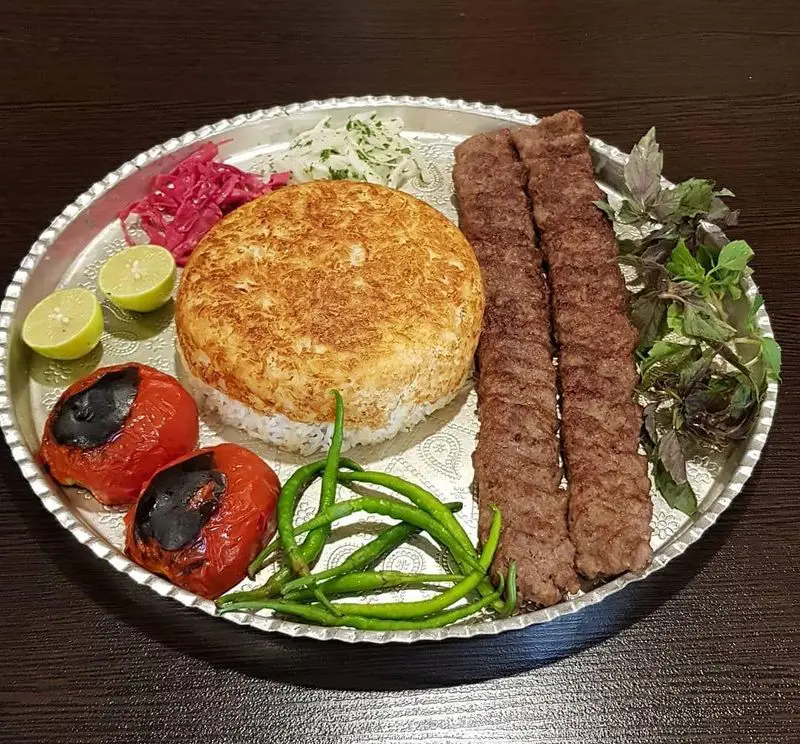 کباب کوبیده اصیل و ته دیگ برنج زعفرانی به همراه گوجه کبابی، لیمو و سبزی تازه. غذای سنتی ایرانی رستوران هانی مطهری.