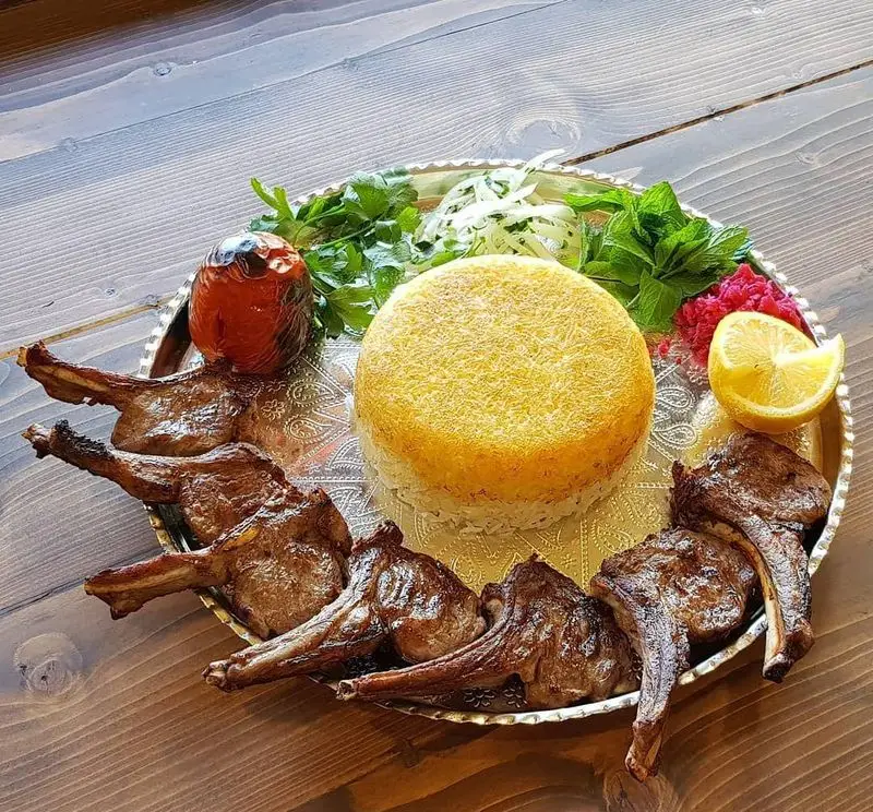 شیشلیک اصیل ایرانی رستوران هانی مطهری با ته دیگ زعفرانی، گوجه کبابی، سبزیجات تازه و لیمو. لذت غذای سنتی.