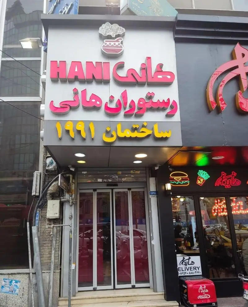 نمای جذاب و روشن رستوران هانی در منطقه مطهری تهران با تابلوی صورتی رنگ، ورودی شیشه‌ای و لوگوی خاص آن.