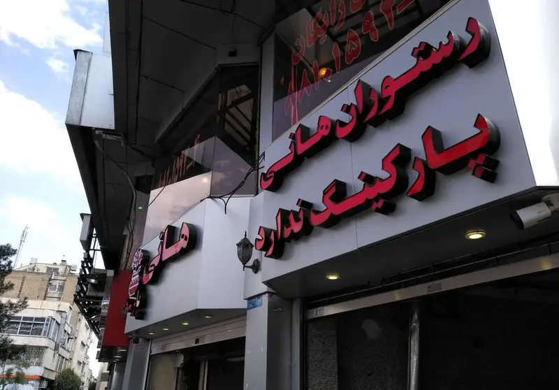 نمای بیرونی رستوران هانی مطهری با تابلوی برجسته قرمز رنگ، شامل اطلاعات 'پارکینگ ندارد'، در یک روز ابری و شلوغ.