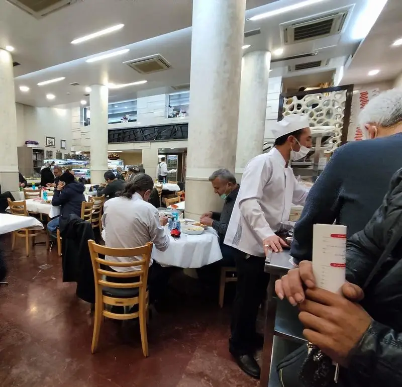 فضای داخلی رستوران هانی مطهری در تهران، نمایشگر مشتریان در حال صرف غذا و کارکنان در حال خدمت‌رسانی در محیطی دلنشین.