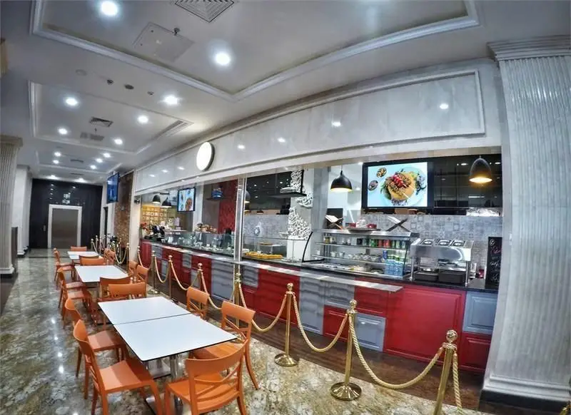 فضای داخلی رستوران ایرانی لتیر با میز و صندلی‌های نارنجی، کانتر سلف سرویس و نمایشگرهای غذا. محیطی مدرن و روشن برای صرف غذا.