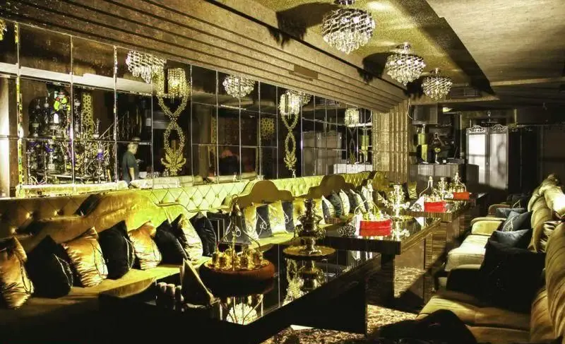 تصویری از طراحی داخلی لوکس کافه رستوران هترا، با مبلمان مخملی طلایی، آینه‌های تزئینی و قلیان‌های شیک. مکانی مجلل.