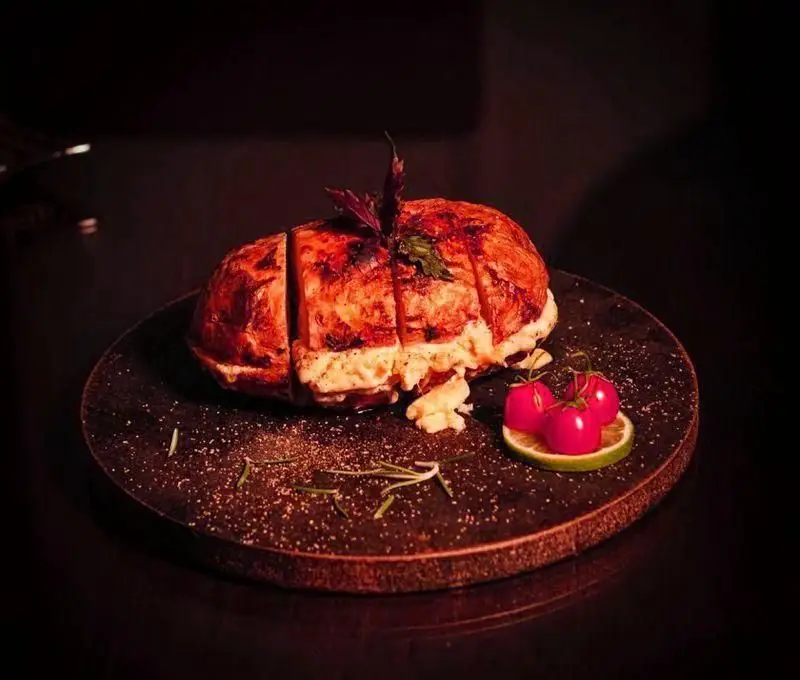 عکس باکیفیت از خوراک ویژه و لذیذ کافه رستوران هترا: یک غذای شکم‌پر برشته و برش‌خورده، همراه با گارنیش گوجه گیلاسی و لیمو.