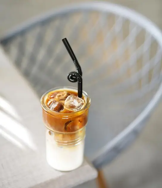آیس لاته جذاب و خنک کافه لیژ با لایه‌های شیری و قهوه‌ای، همراه با یخ و نی مشکی، یک نوشیدنی ایده‌آل برای تابستان و آرامش.