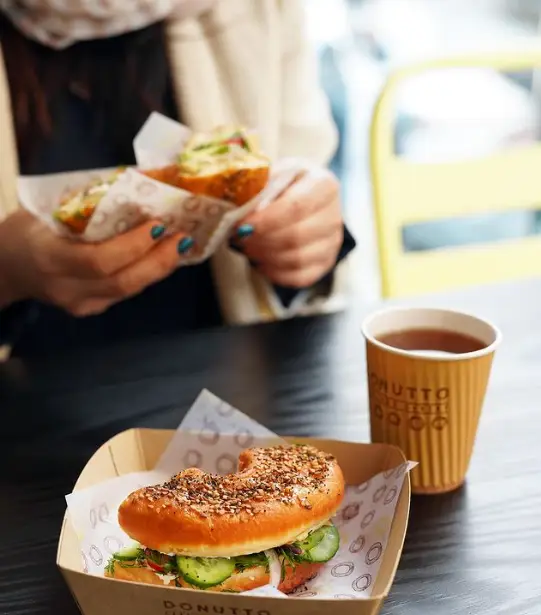 مشتری در کافه لیژ در حال لذت بردن از ساندویچ بگِل تازه با سالمون و خیار، همراه با یک فنجان چای گرم.